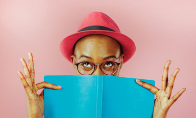 woman in red hat holds blue book over face